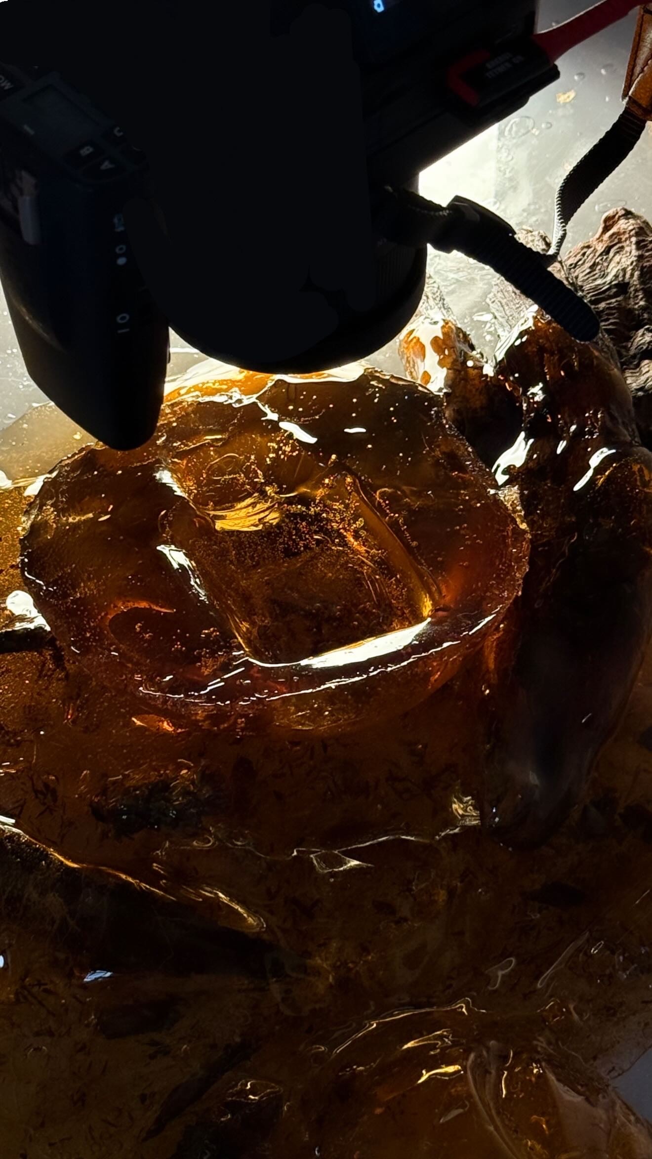 A camera positioned close above the illuminated amber and oud material set for Dior Sauvage Extrait.