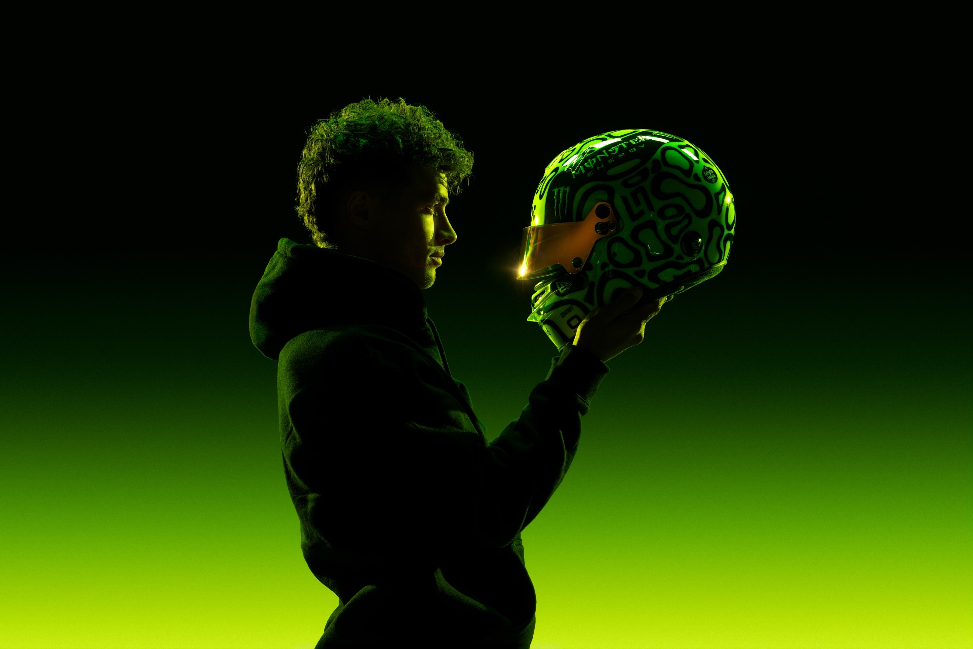 Lando Norris photographed by George Kroustallis holding his Monster Energy racing helmet against a black-to-neon-green campaign environment.
