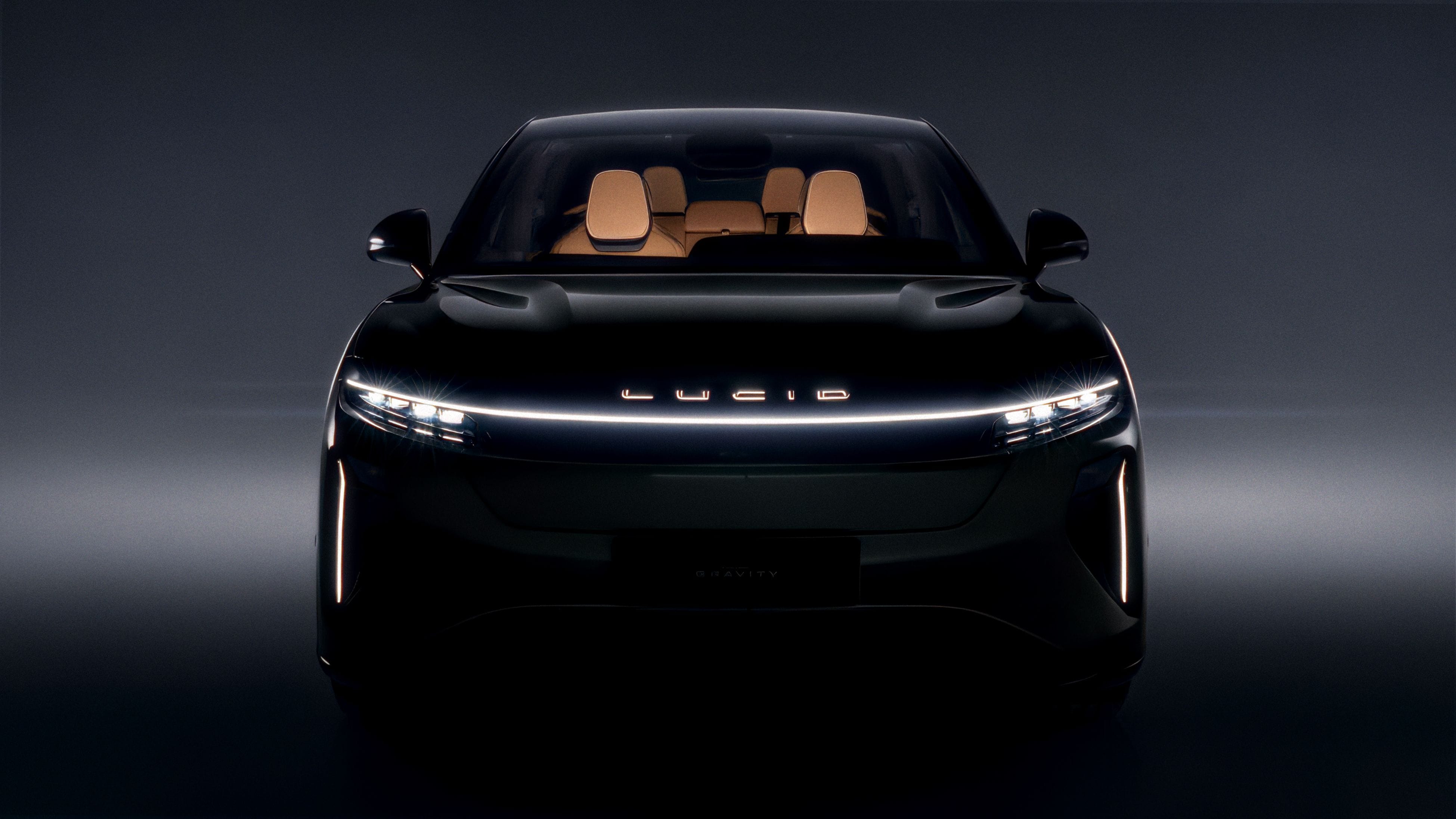 Front view of a black Lucid Gravity emerging from darkness in the Lucid Motors × Hypebeast campaign, with its continuous light bar and tan interior illuminated.