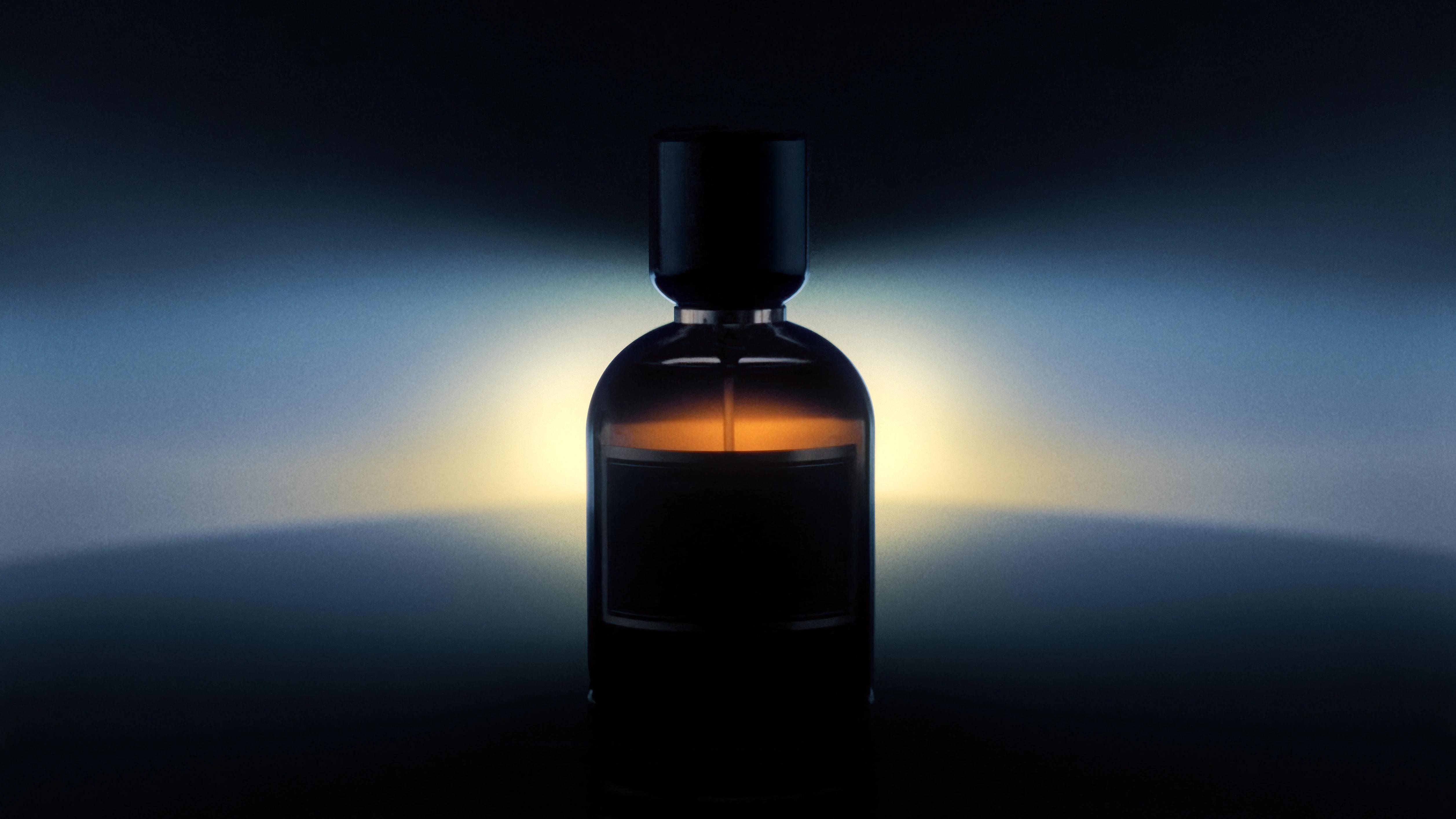 Buio perfume bottle silhouetted against a cold blue field with a low amber glow behind the glass.