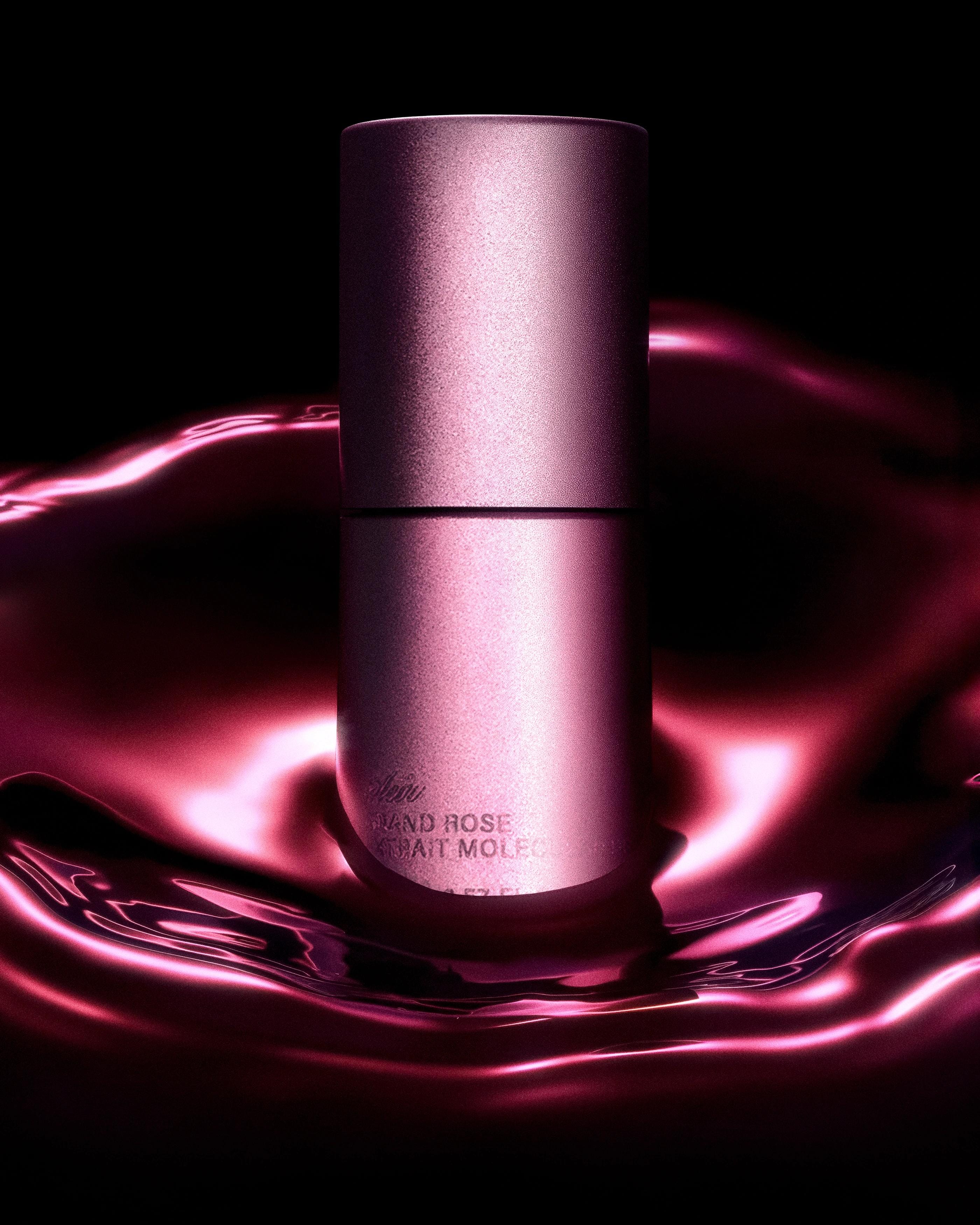 Rose-coloured Aeir fragrance atomiser rising from a glossy magenta liquid surface against black.