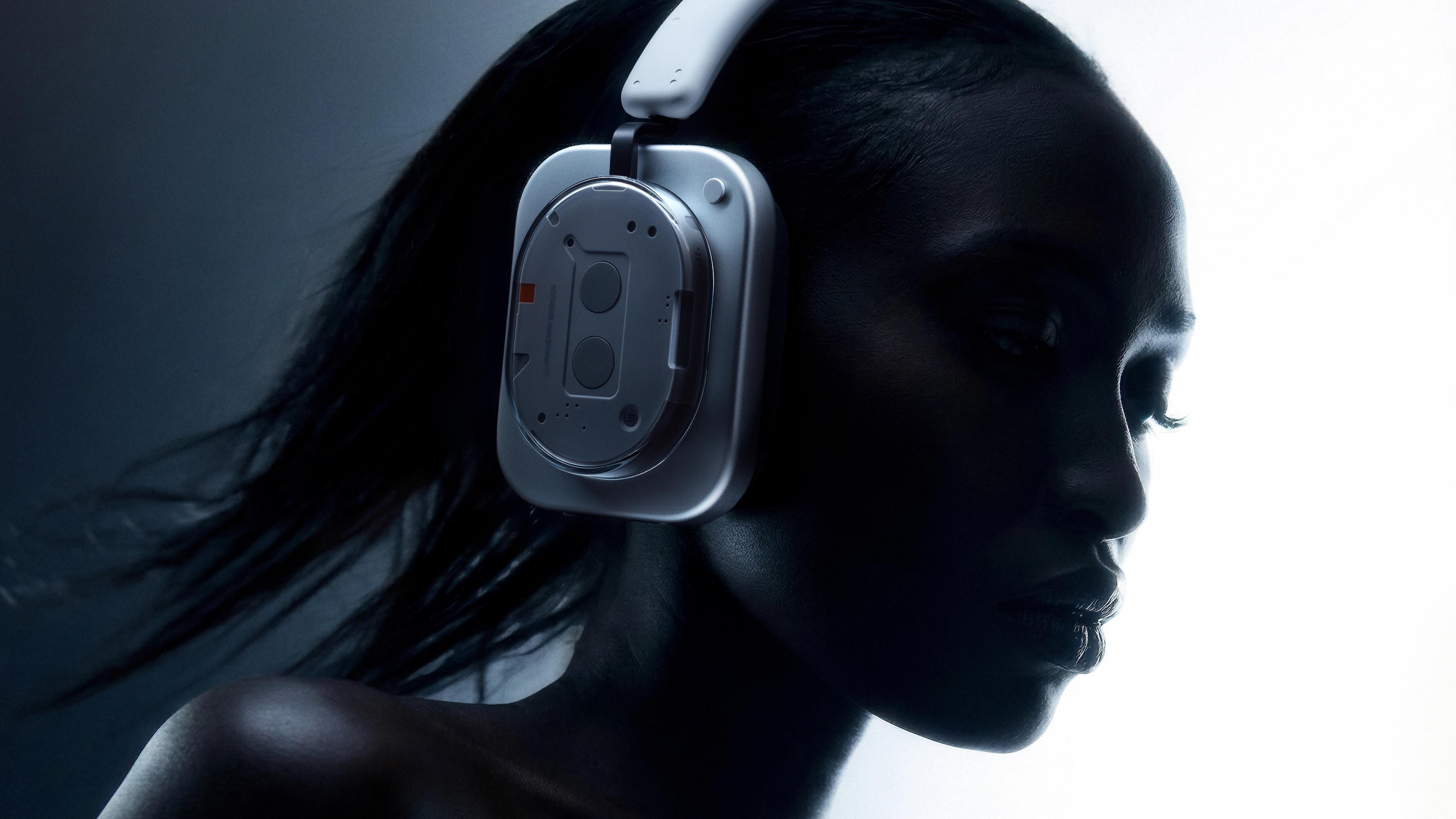 Side-profile portrait of a model wearing silver Nothing Headphone (1) in cool blue-white light.