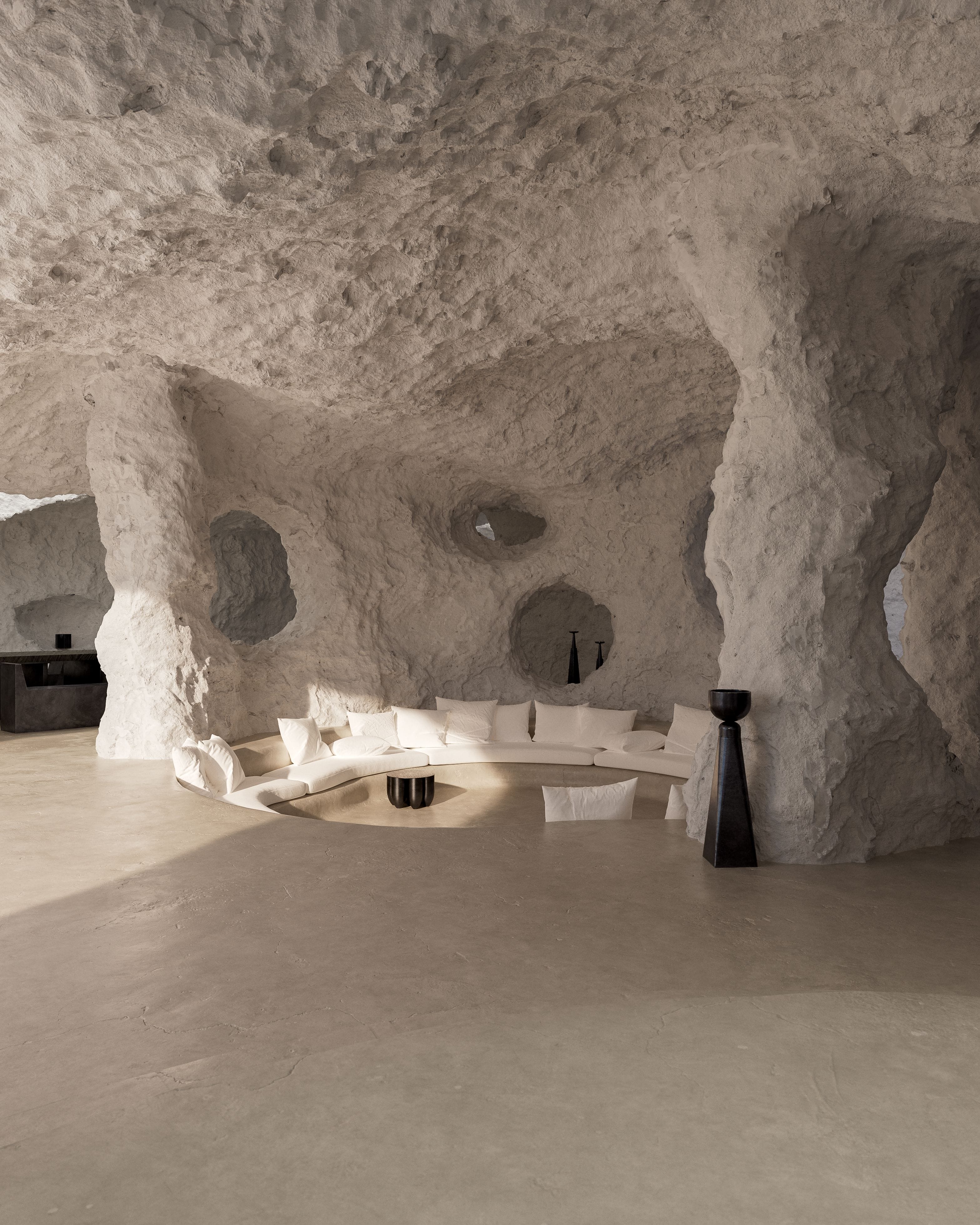 Carved white-rock living room with a curved cream sofa, low circular table and tall black vessel.