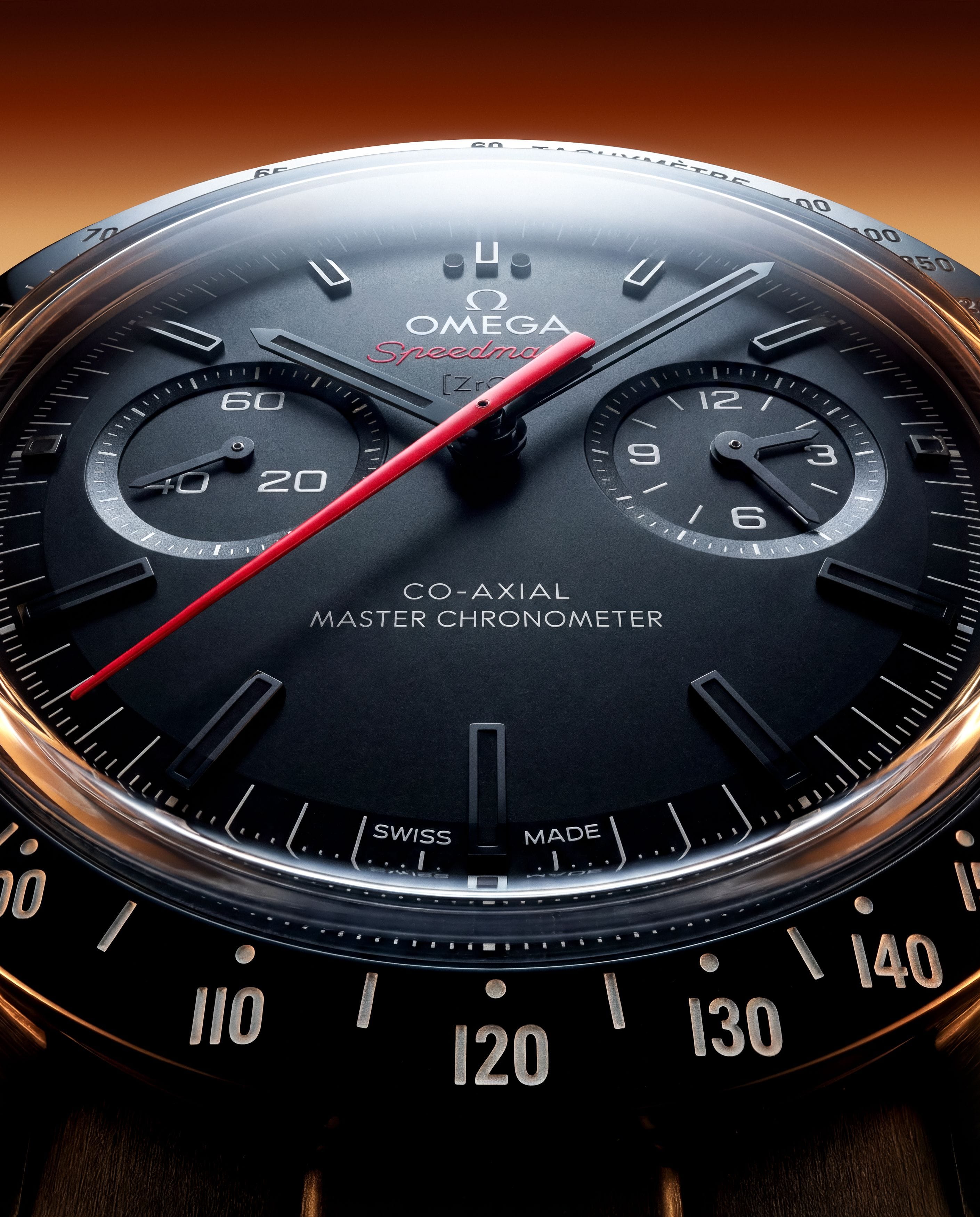 Extreme ant’s-eye close-up of the black Omega Speedmaster, magnifying its domed crystal, tachymeter and red chronograph hand.