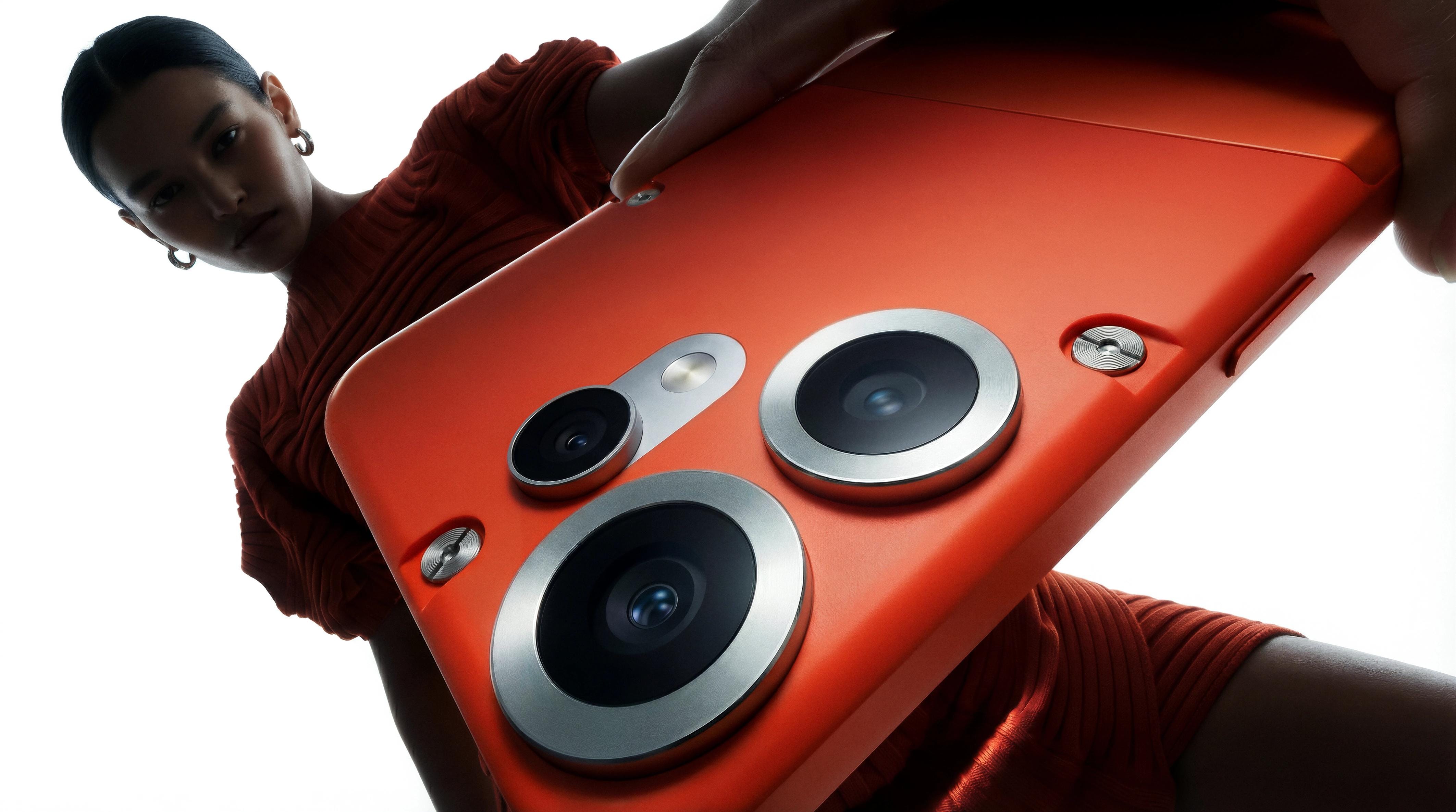 Low-angle portrait of a model behind an oversized orange CMF Phone 2 Pro.