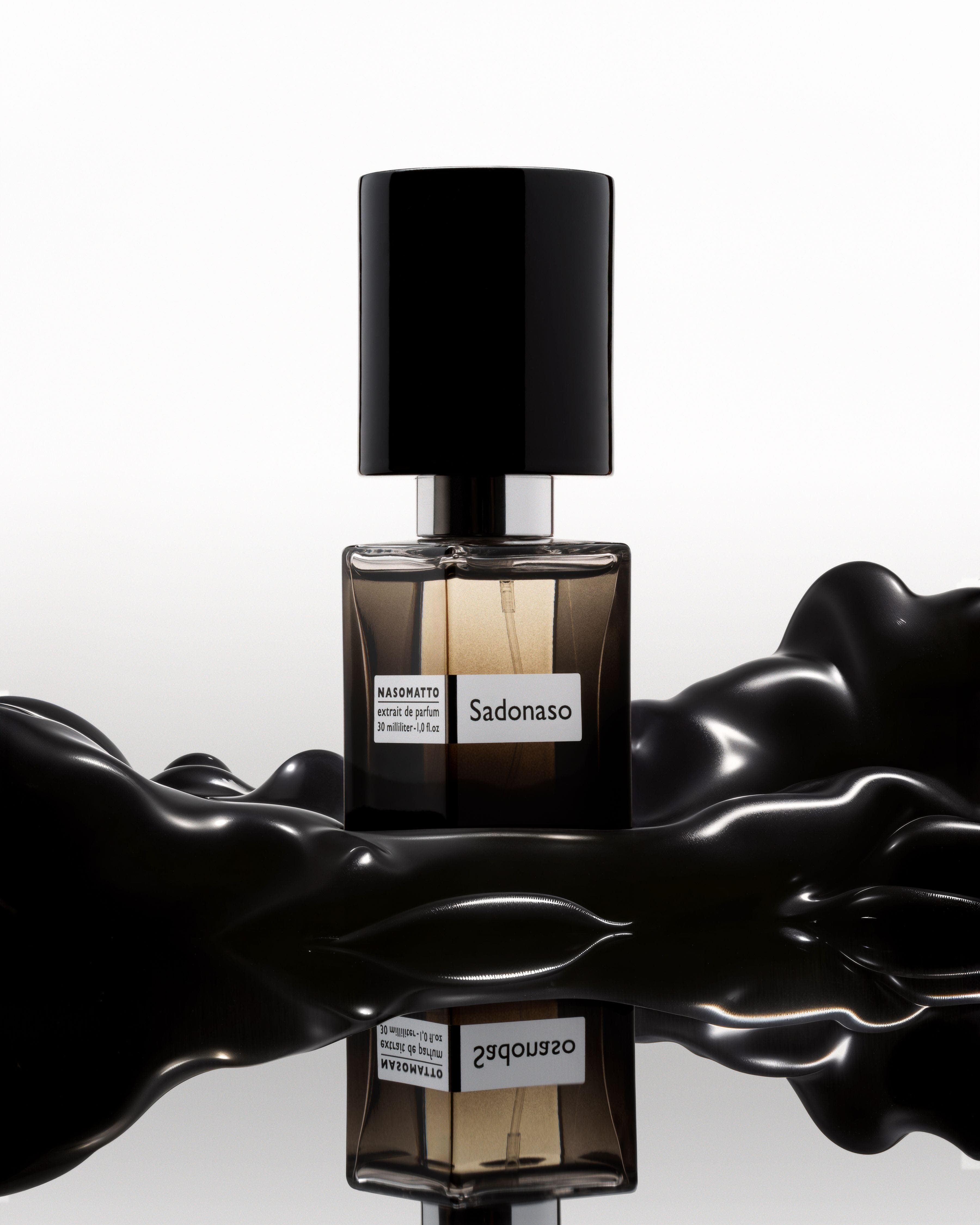 Nasomatto Sadonaso perfume bottle standing between glossy black liquid forms on a reflective white surface.