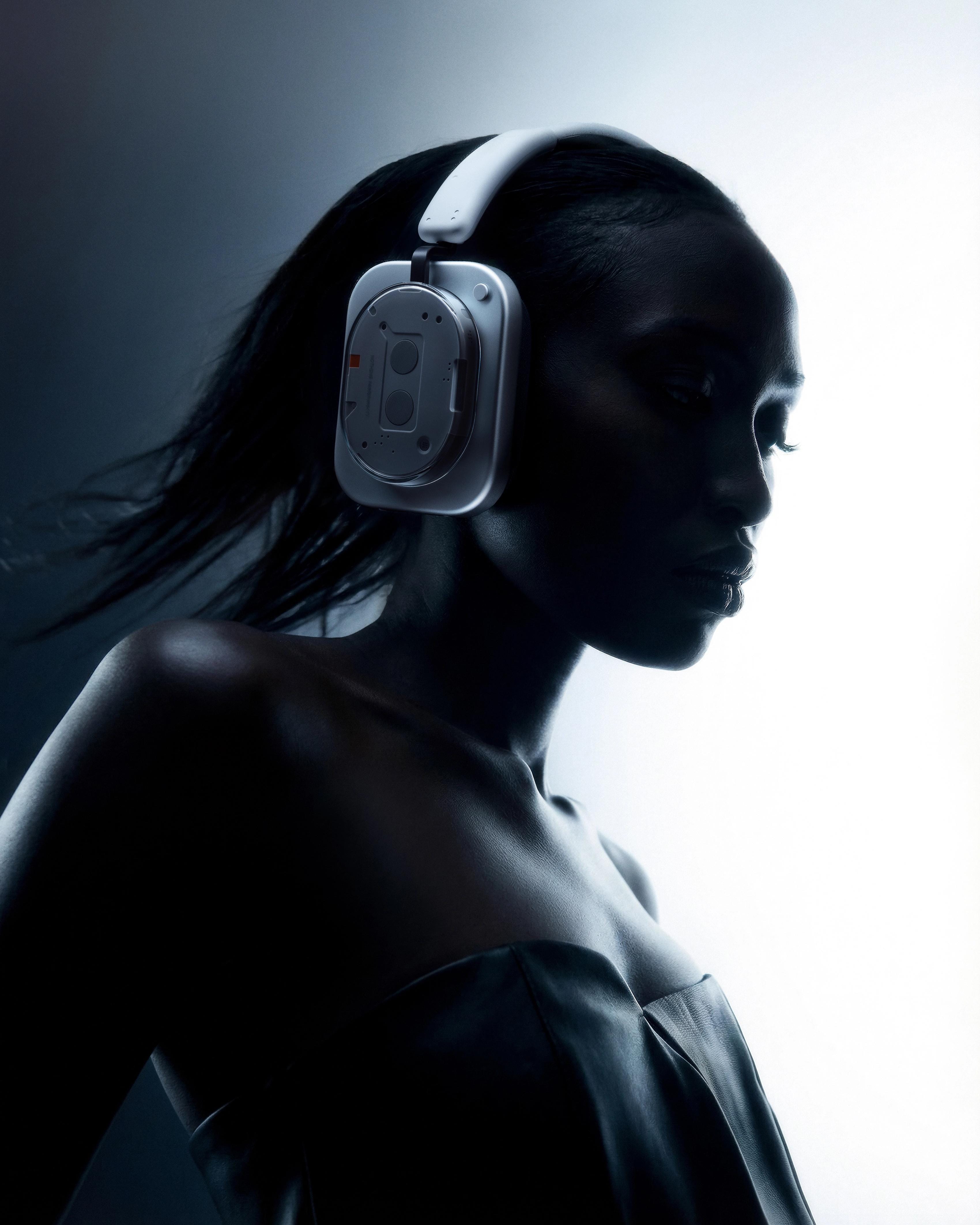 Vertical side-profile portrait of a model in a metallic strapless garment wearing silver Nothing Headphone (1), lit in cool blue-white tones.