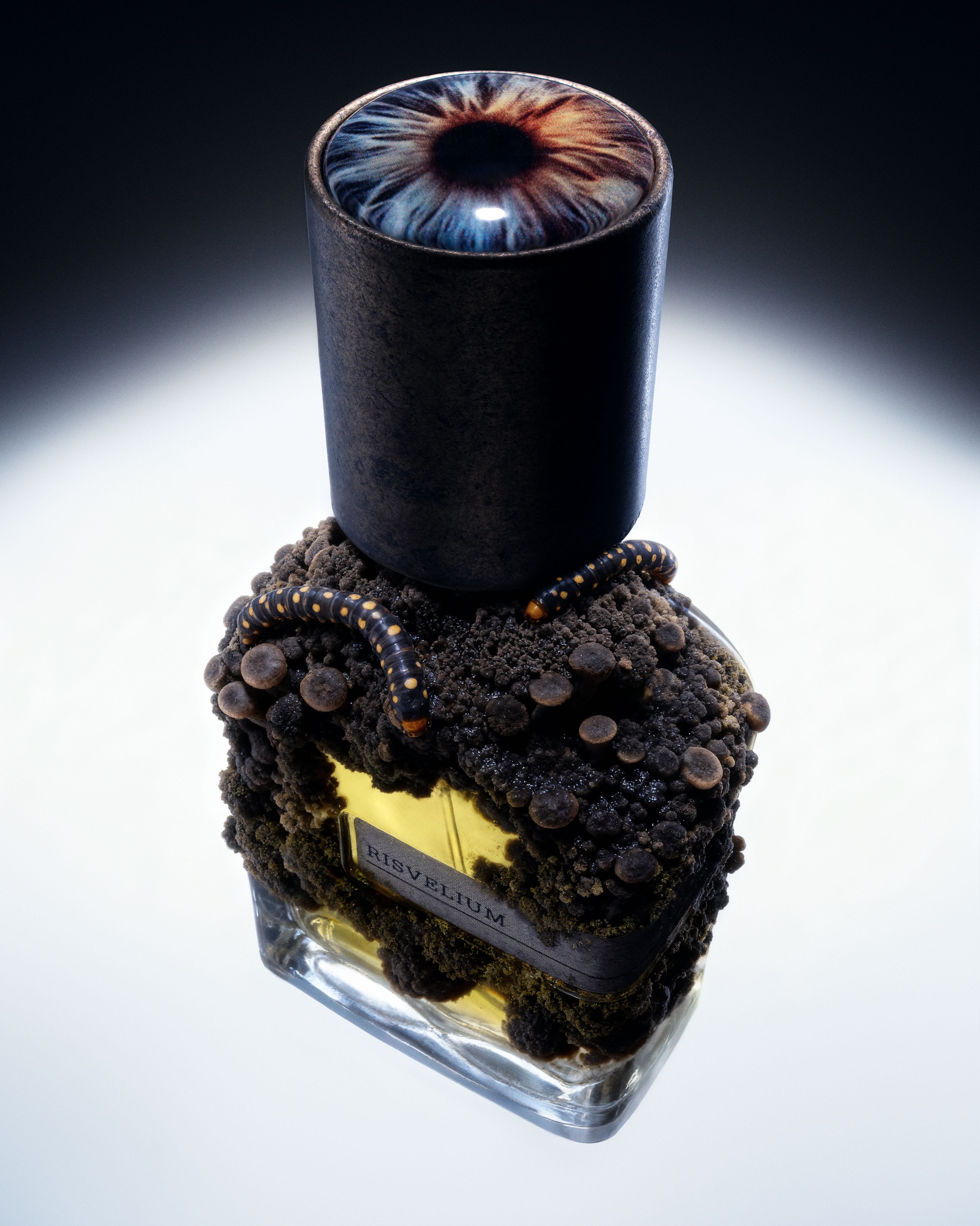 Orto Parisi Risvelium perfume bottle covered in dark organic clusters, topped with an iris-like cap and lit from below.