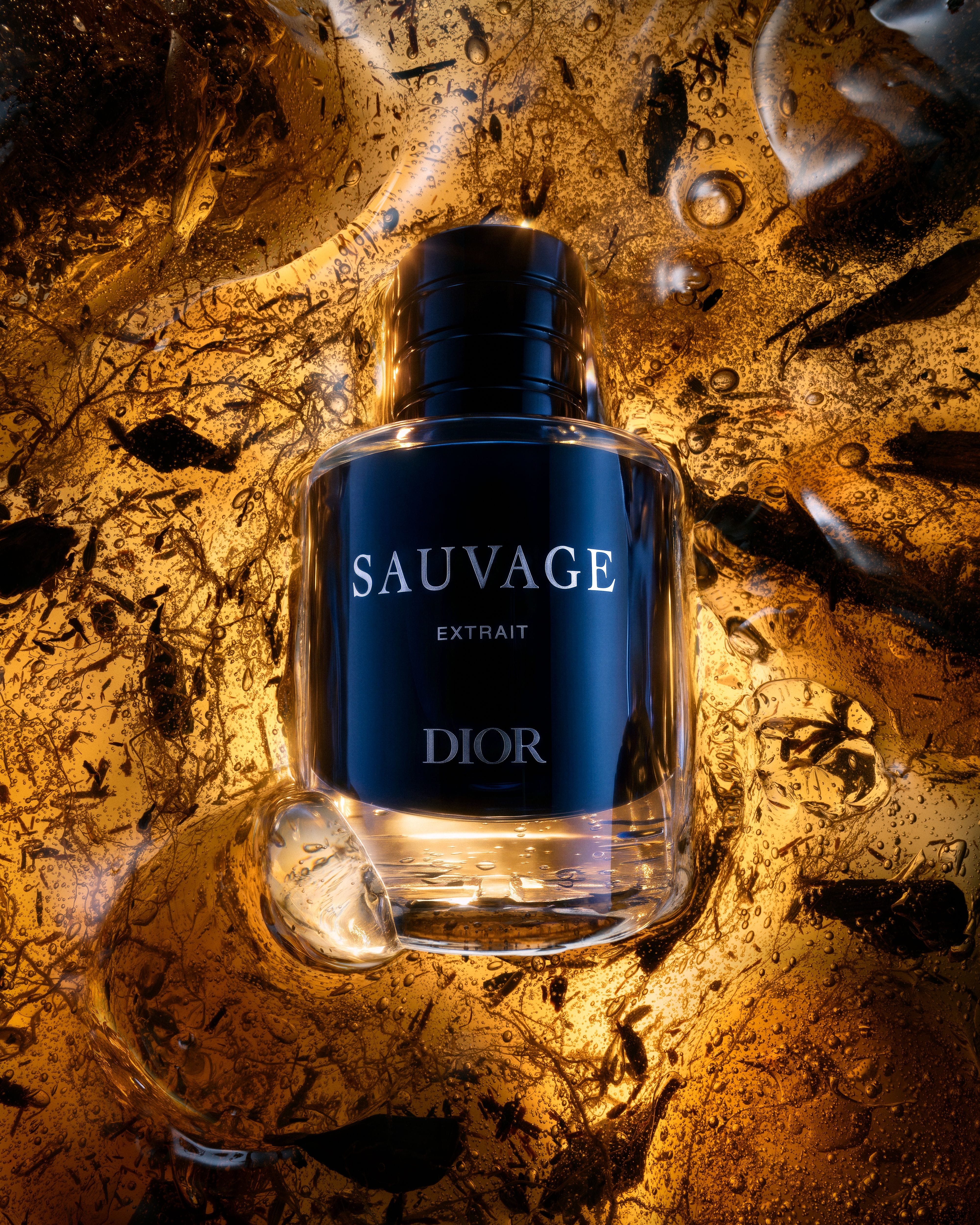 Dior Sauvage Extrait bottle surrounded by illuminated amber material, suspended bubbles and dark fragments.
