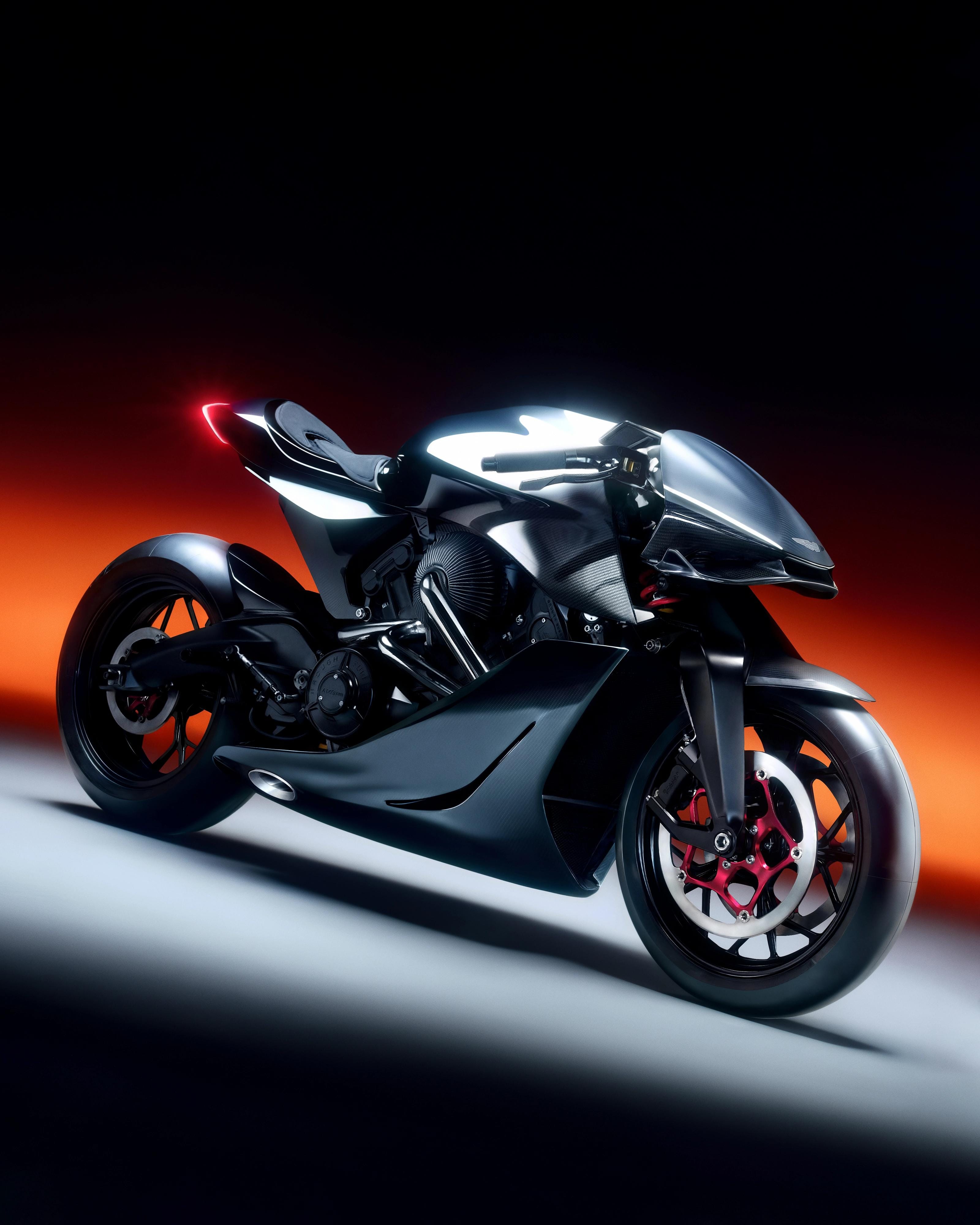 Three-quarter studio portrait of the black AMB 001 motorcycle against red-orange and white light.